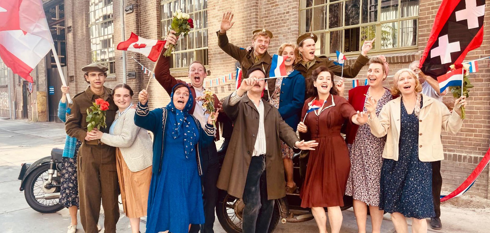 Foto van acteurs in naoorlogse kleding met Amsterdamse vlag na bevrijding door Canadezen in 1945.